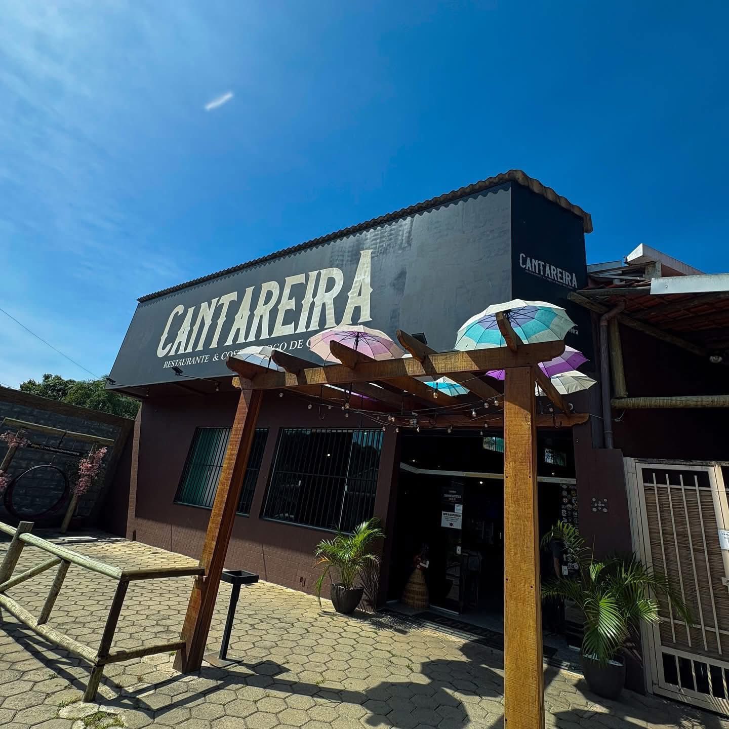 Fachada ensolarada do Restaurante Cantareira, com a placa da casa e as sombrinhas na entrada